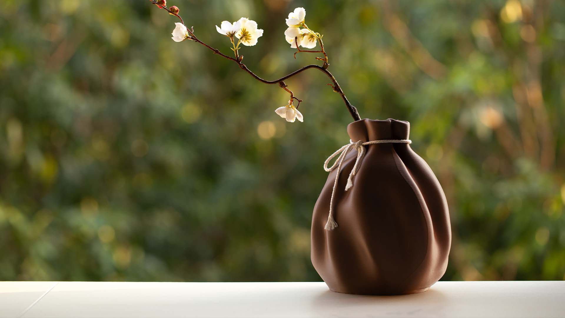 A 3D printed vase that mimics the shape of fabric, placed on the balcony, paired with green landscape, brings a fresh and calm feeling.