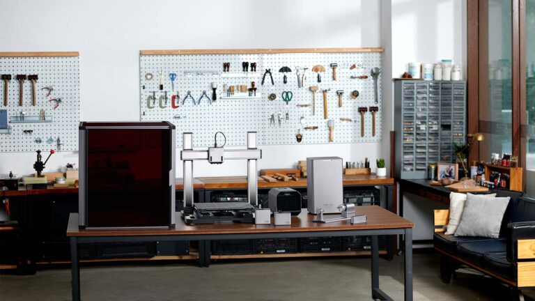 A well-organized workshop featuring a large 3D printer and other equipment on a sturdy wooden table. The background showcases pegboards with an assortment of neatly arranged tools, including hammers, screwdrivers, and wrenches. Shelves and cabinets hold additional supplies, while a modern couch with a cushion sits in the corner near a window, allowing natural light to brighten the space.